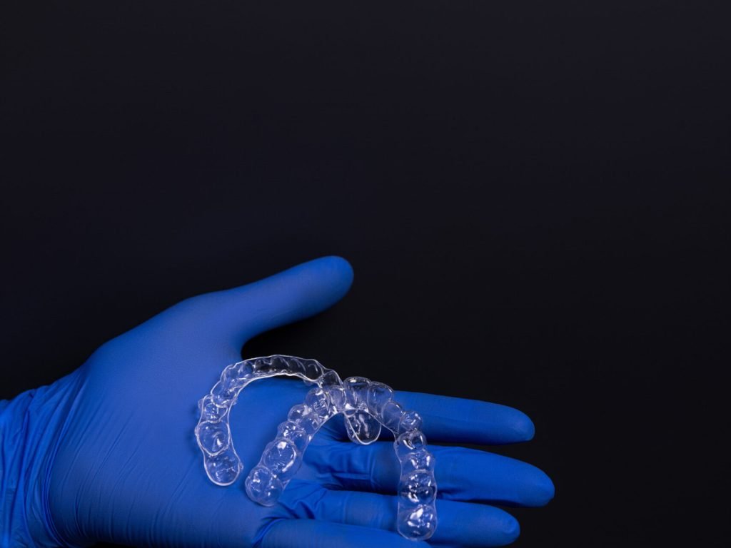 A dentist in blue rubber gloves holds transparent plastic aligners, which are devices used to correct bite alignment in adult patients at the dental clinic in the hospital. The dental aligners are against a black background. High quality photo