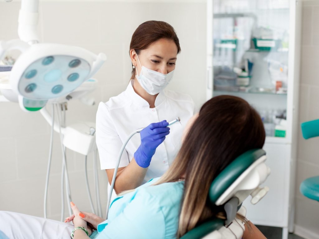 Woman dentist treats a patient. A woman in a mask sits in a dental chair in the clinic. Woman dentist treats a patient. A woman in a mask sits in a dental chair in the clinic.